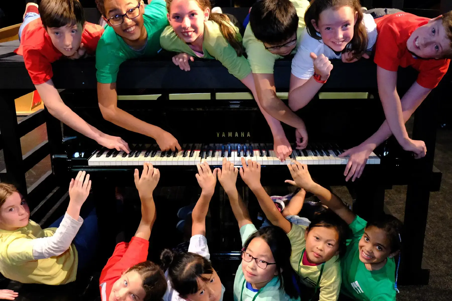 Group of children gathered around a grand piano during a creative educational initiative — capturing the energy and inclusivity of a national youth music campaign