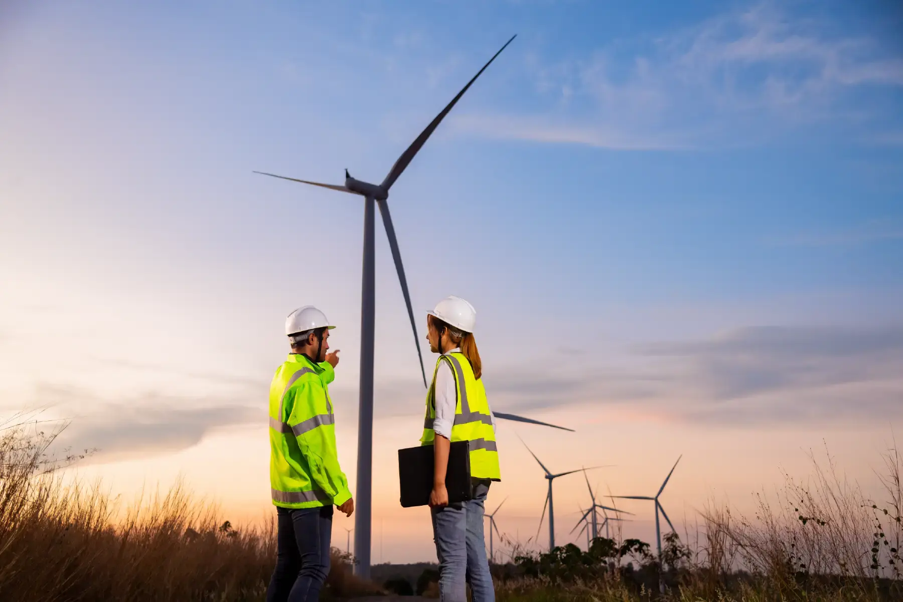 Field engineers in safety gear inspecting wind turbines at a renewable energy site