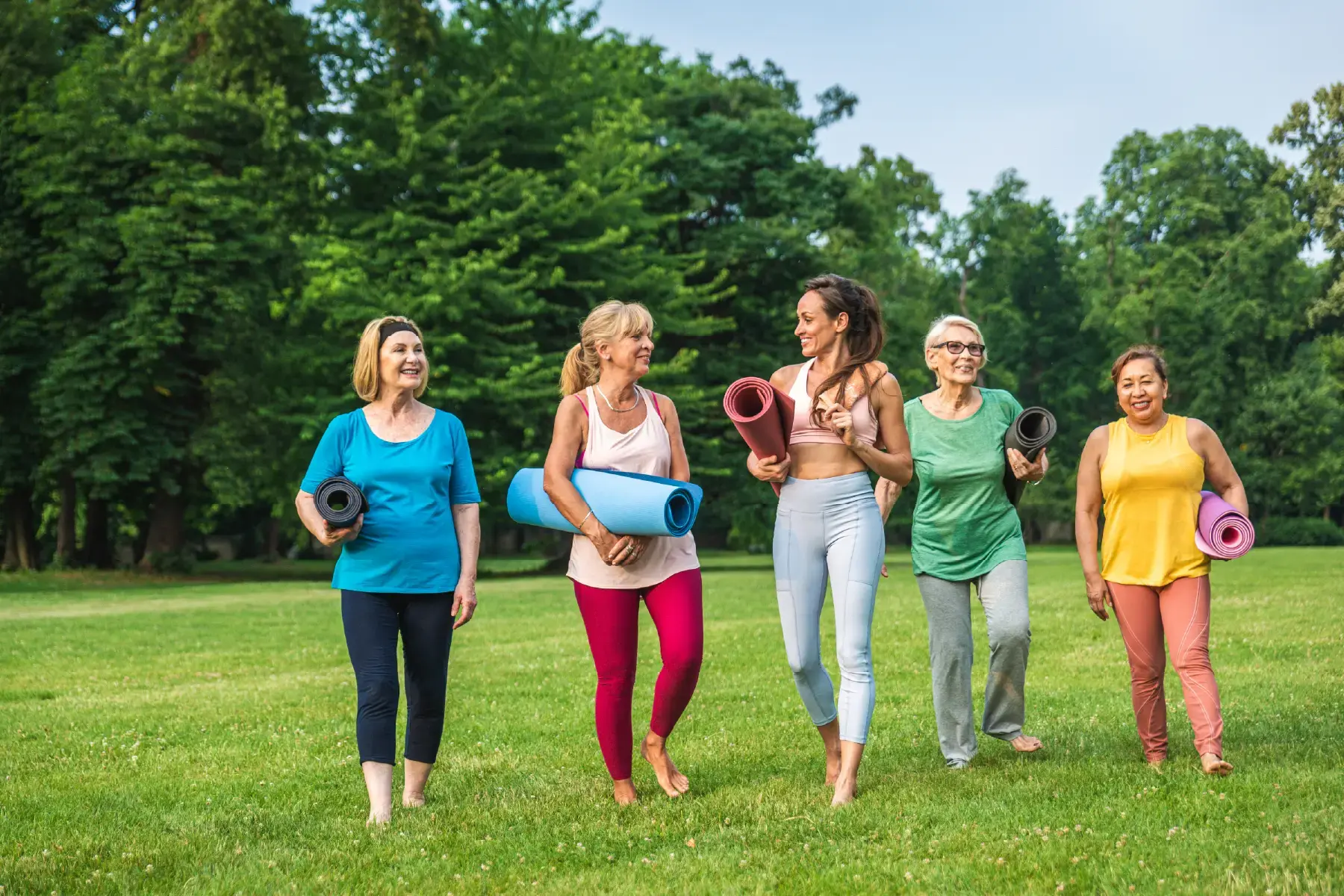 Group of women walking with yoga mats in a park, symbolising the community and lifestyle aspects of the wellness sector