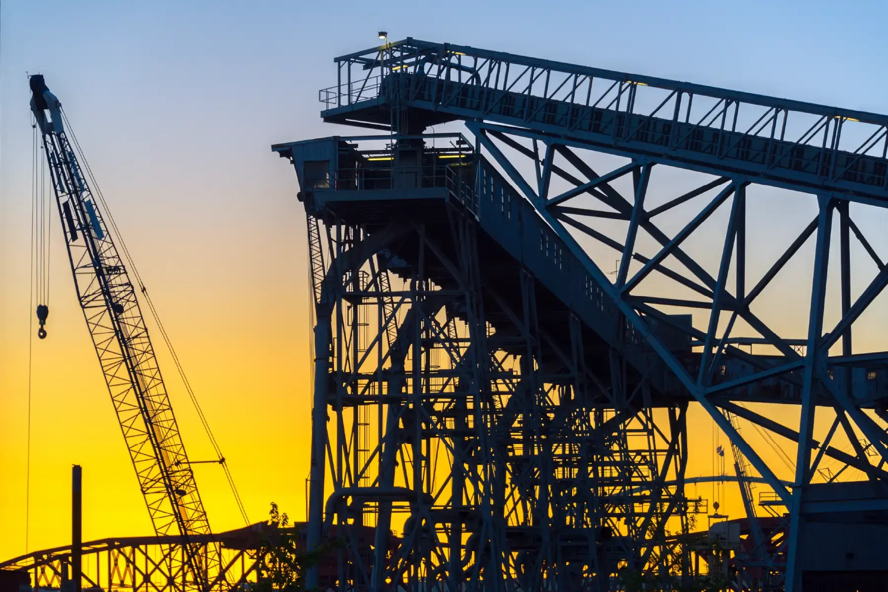 Heavy steel infrastructure and cranes silhouetted at sunset, representing industrial and infrastructure sectors Heavy steel infrastructure and cranes silhouetted at sunset, representing industrial and infrastructure sectors